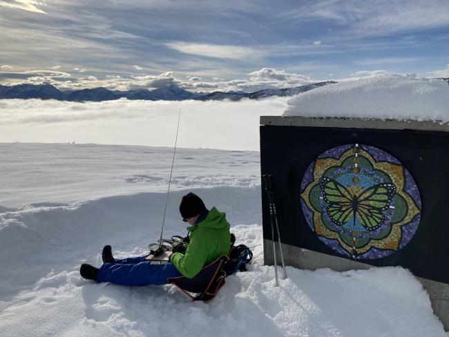 Me, seated in the snow, logging, with low clouds and mountains in the background