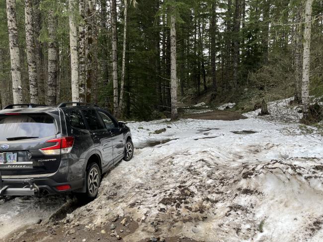 Car stuck  in drift of wet snow in a dip in on a gravel road in the forest