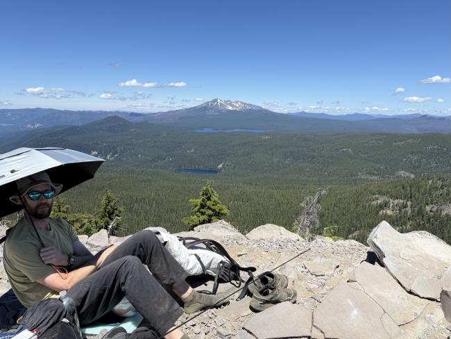 Summit chilln Man with umbrella relaxing on summit with mountain view in background